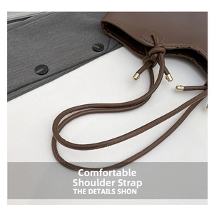 Detail of a brown leather tote with drawstring closure and golden metal accents