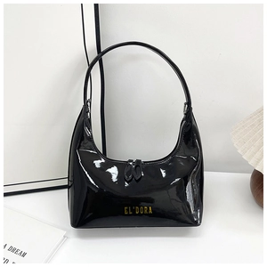 Detail of glossy black patent leather shoulder bag with golden logo in a chic setting