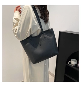 Minimalist black tote bag shown on model's shoulder with beige trench coat for casual look