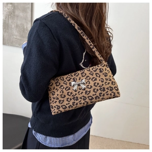 Detail of leopard print shoulder bag with a metallic silver butterfly clasp on textured fabric