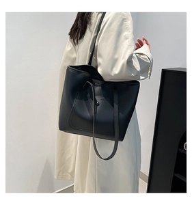 Minimalist black leather tote bag with thin double straps worn by model in a studio