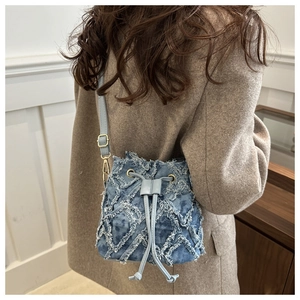 Vista laterale borsa a secchiello in denim con bordi sfrangiati e chiusura a coulisse