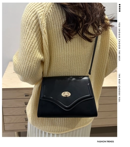Detail of a black leather crossbody bag with a golden twist lock on a knit sweater backdrop