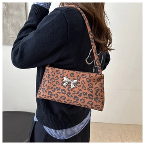 Detailed view of leopard print baguette bag featuring a silver metal butterfly ornament
