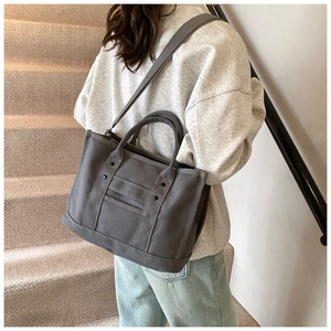 Close-up of a dark grey canvas tote bag with functional pockets and metal rivets