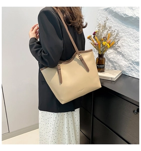 Close-up of beige tote bag with dark brown trim and adjustable leather strap on model
