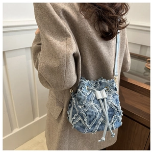 Dettaglio della borsa a secchiello in denim con bordi sfrangiati e coulisse indossata