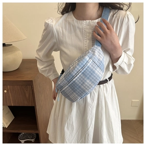 Close-up of blue gingham chest bag with adjustable strap worn on a white dress