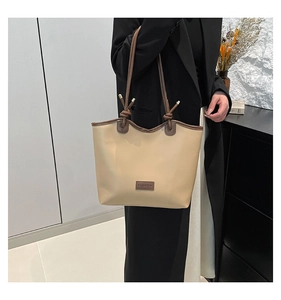 Detail of beige tote bag with brown leather trim, knot handles, and fashion label