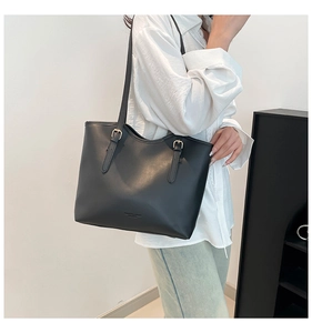 Detail view of the black matte leather tote bag featuring a gold buckle on the shoulder strap