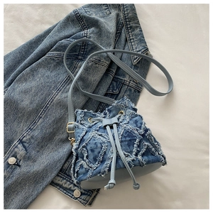 Dettaglio della borsa a secchiello in denim trapuntato con bordi sfilacciati e coulisse