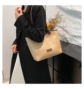 Detail view of large beige tote bag with brown straps worn over a black blazer