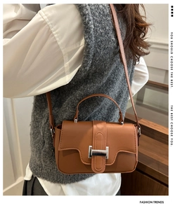 Detail of a brown leather crossbody bag featuring a silver square buckle and top handle