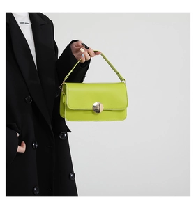 Détail du sac baguette vert citron avec boucle ronde argentée sur un blazer noir