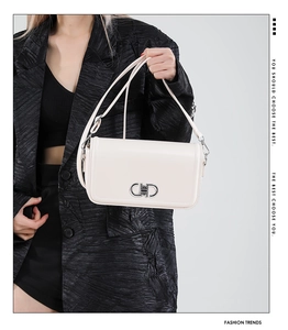 Detail of a minimalist cream white leather handbag with a silver metal clasp on black suit