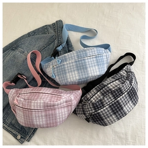 Detailed view of plaid corduroy waist bags in blue, pink, and grey on a fabric backdrop