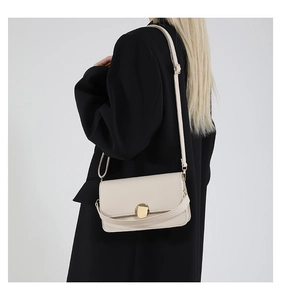 Détail du sac bandoulière crème avec boucle dorée porté sur un blazer noir chic