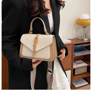 Detail of a two-tone woven crossbody bag with gold buckle and wide fabric strap