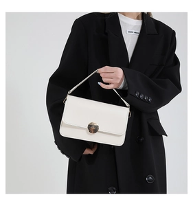 Détail du sac carré en cuir blanc crème avec boucle en métal doré sur blazer noir
