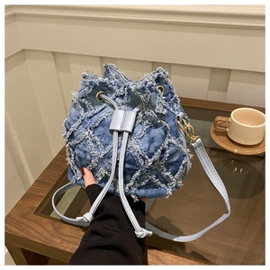 Dettaglio della borsa a secchiello in denim blu con bordi sfrangiati e hardware oro