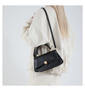 Detail of a minimalist black leather baguette bag with a golden square metal buckle