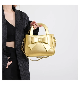Detail of elegant gold crossbody bag featuring large bow design and sturdy metal handle