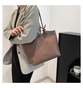 Detail of dark brown tote bag with FASHION patch and slim shoulder straps on a model