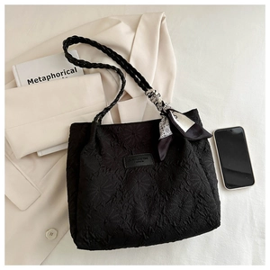 Detail of black tote bag with floral embossing, woven strap and decorative silk scarf
