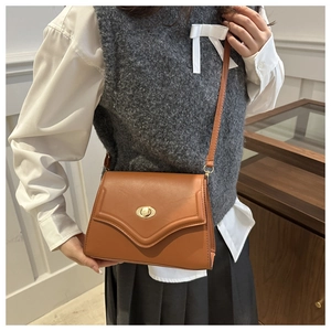 Detail of a brown leather envelope crossbody bag with a golden circular twist lock