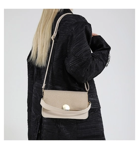 Detail of a beige patchwork crossbody bag with woven texture and round metal buckle