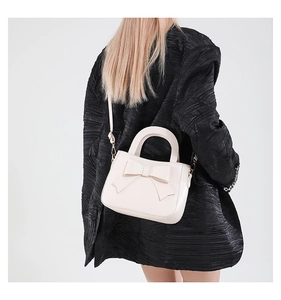 Elegant cream bow handbag worn over a black textured top for a stylish minimal contrast