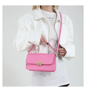 Detail of pink leather crossbody bag with round gold metal buckle and thin shoulder strap