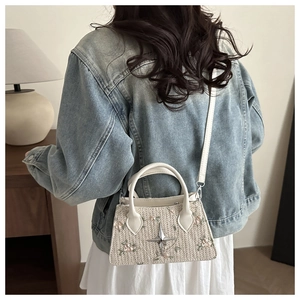 Detail of crossbody straw bag with floral embroidery and star charm on female model