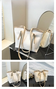 Detail view of off-white leather tote bag with adjustable brown strap and logo