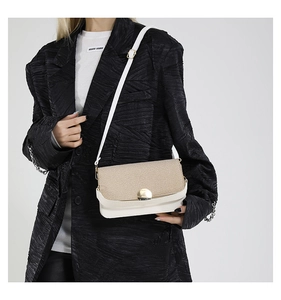 Détail d'un sac bandoulière blanc avec rabat en paille tressée et boucle dorée ronde