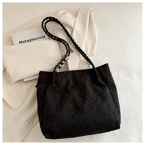 Detail of black tote bag with textured fabric, woven handles and decorative scarf