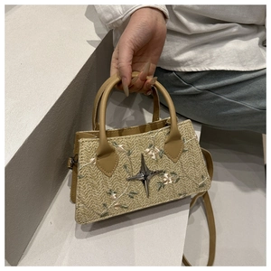Dettaglio della borsa in paglia intrecciata con ricami floreali e stella d'argento