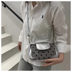 Détail du sac bandoulière argenté avec motif à pois et logo texturé gravé sur le rabat