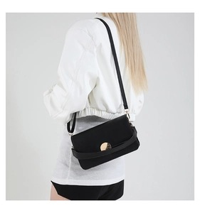 Detail of a black crossbody bag with gold buckle and textured strap on a model