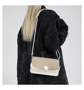 Vue latérale du petit sac bandoulière en paille tressée et cuir blanc sur manteau noir