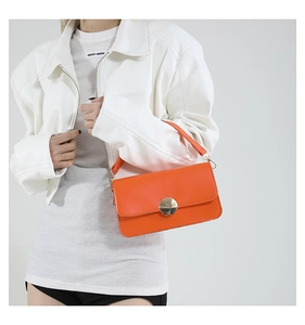 Détail du sac à bandoulière orange vif avec une grande boucle en métal doré et du cuir fin