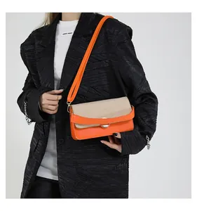 Detail of a bright orange leather and woven crossbody bag worn over a black blazer