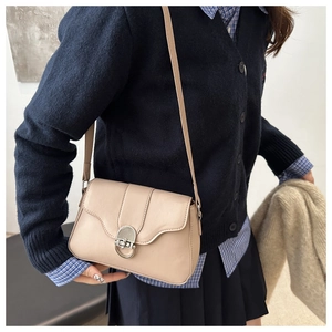 Detail of beige crossbody flap bag with silver metal swivel lock on a model's shoulder