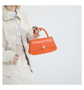 Close-up of bright orange crossbody bag with gold buckle on a cream outfit
