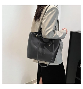Detail of minimalist black leather tote bag featuring a FASHION label and knotted shoulder strap