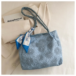 Detail of light blue quilted tote bag with floral embroidery and decorative silk scarf
