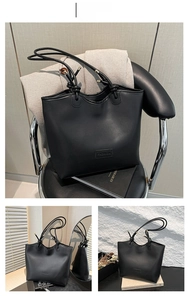 Close-up of black tote bag featuring a leather fashion label and metal strap details