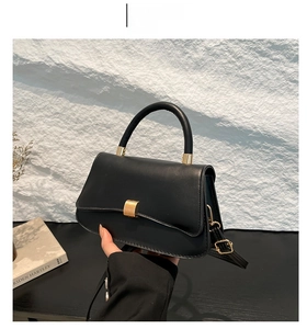Detail of black lychee texture handbag with golden curved clasp and adjustable strap