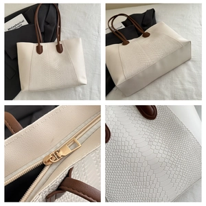 Detail view of white tote bag showing gold zipper and embossed crocodile leather texture