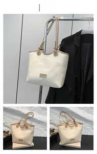 Detail view of a white tote bag with tan handles and a rectangular fashion patch